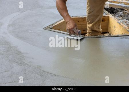 Un operatore di costruzioni che utilizza un bordatore in acciaio inossidabile su un angolo di formatura in cemento umido per un nuovo pavimento in cemento Foto Stock