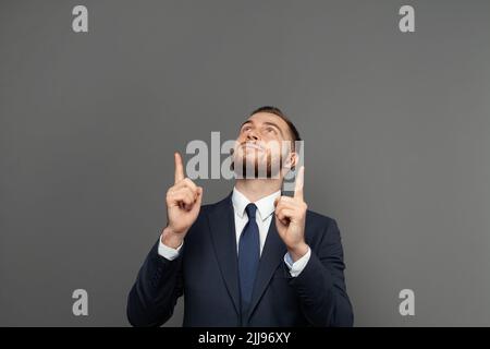 Ritratto di un uomo d'affari felice puntando le dita su sfondo grigio Foto Stock