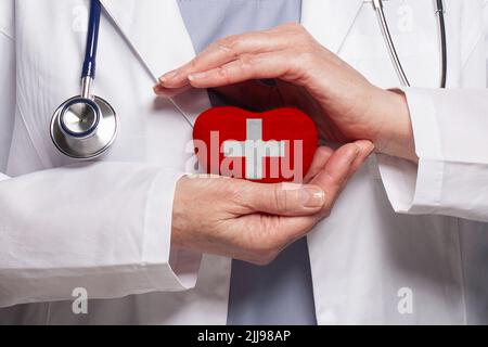 Medico svizzero che tiene il cuore con la bandiera di fondo della Svizzera. Concetto di assistenza sanitaria, beneficenza, assicurazione e medicina Foto Stock
