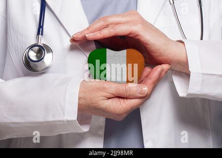 Medico irlandese che tiene il cuore con bandiera di fondo irlandese. Concetto di assistenza sanitaria, beneficenza, assicurazione e medicina Foto Stock