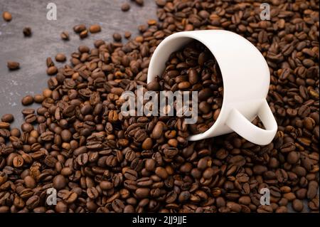 Una tazza di caffè capovolta con i chicchi di caffè versati su una superficie metallica con i chicchi di caffè versati su di essa. Foto Stock