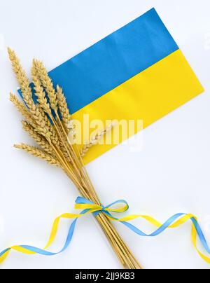 Spikelets di grano e nastri in colori della bandiera Ucraina su sfondo chiaro. Concetto di scarsità di cibo globale a causa della guerra in Ucraina Foto Stock