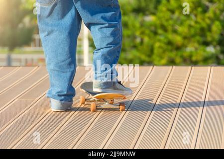 Ragazzo in jeans blu e sneakers si alza sul pavimento con uno skateboard che mette il piede su di esso Foto Stock