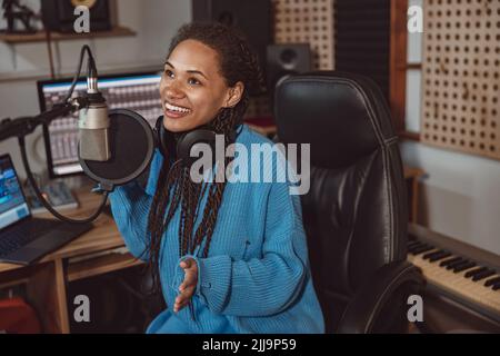 African cute donna blogger registra podcast utilizzando le cuffie e parlare in microfono in studio di musica professionale Foto Stock