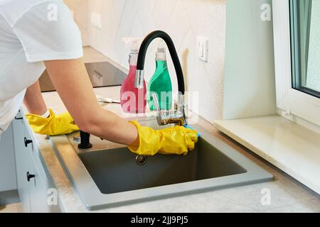 Donna acqua di pulizia rubinetto al lavandino in cucina Foto Stock