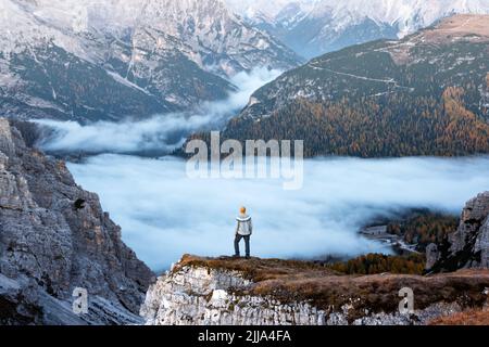 Un turista si erge sulla nebbia ai margini di una scogliera delle Dolomiti. Dove si trova Auronzo rifugio nel Parco Nazionale delle tre Cime di Lavaredo, Dolomiti, Trentino Alto Adige, Italia Foto Stock