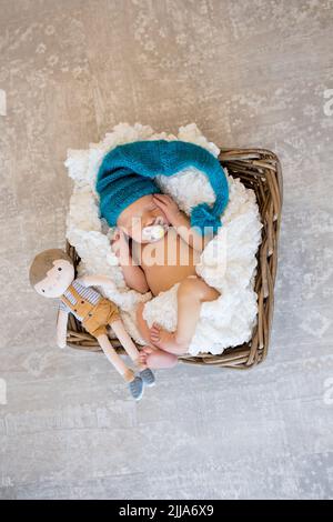 Un bambino neonato in un cappello di maglia blu dorme tranquillamente con un giocattolo in un cestino Foto Stock