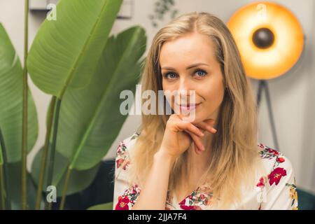 Concetto di cura della pelle. Ritratto di una bella ragazza caucasica bionda a metà del 20s che tocca il mento. Pianta con grandi foglie sullo sfondo. Foto di alta qualità Foto Stock