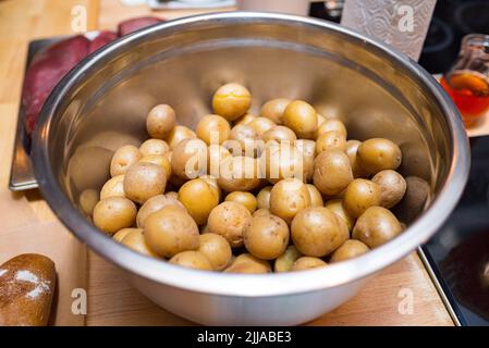 Una ciotola in metallo profondo di patate crude non pelate prima della cottura. Sul tavolo da cucina. Foto Stock