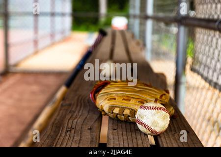 Baseball e guanto su panca in dugout con sfondo sfocato Foto Stock