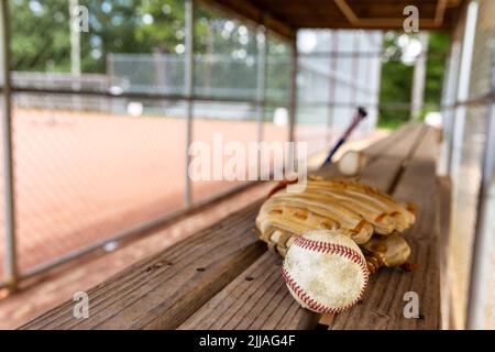 Baseball e guanto su panca in dugout con sfondo sfocato Foto Stock