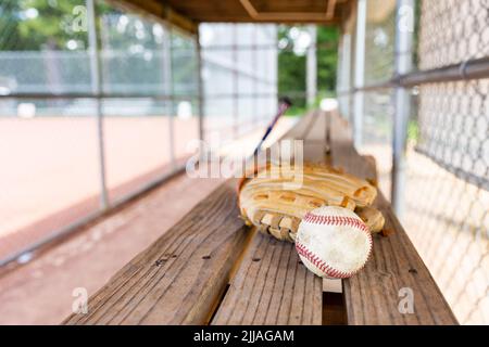 Baseball e guanto su panca in dugout con sfondo sfocato Foto Stock