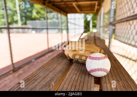 Baseball e guanto su panca in dugout con sfondo sfocato Foto Stock