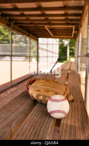 Baseball e guanto su panca in dugout con sfondo sfocato Foto Stock