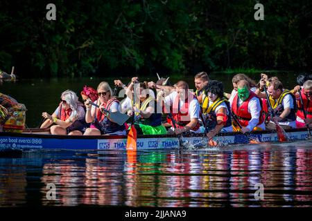 Gruppo di colleghi di lavoro, alcuni in abito fantasia, paddle loro Dragon Boat male Foto Stock