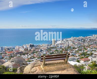 Vista panoramica su una panca pubblica su una scogliera o collina che domina la città e l'oceano. Area naturale vuota, tranquilla e tranquilla con un Foto Stock