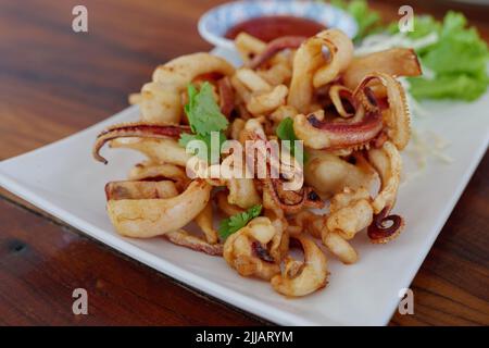 Calamari croccanti fritti, calamari su piatto bianco e salsa piccante sul lato. Foto Stock