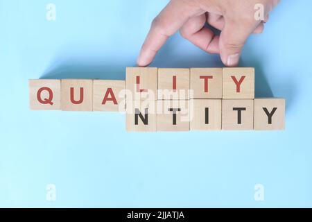 Concetto di qualità rispetto alla quantità. Mano che cambia quantità di parola a qualità su blocchi di legno. Foto Stock