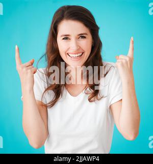 Le cose stanno guardando verso l'alto. Ritratto dello studio di una giovane donna attraente che punta verso l'alto su uno sfondo blu. Foto Stock