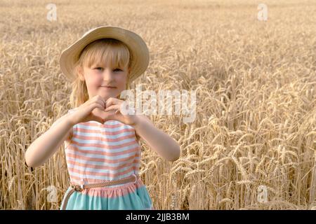 Bionda Girl guarda la macchina fotografica e mostra il cuore delle sue mani nel campo di grano . primo piano Foto Stock