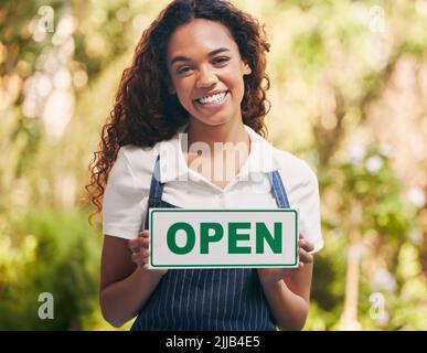 Pronta ad accogliere il pubblico, una giovane donna che porta un cartello con la scritta che il suo vivaio è aperto. Foto Stock