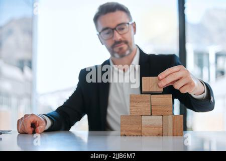 L'innovazione è il catalizzatore del cambiamento: Un uomo d'affari maturo che lavora con blocchi di legno in un ufficio moderno. Foto Stock