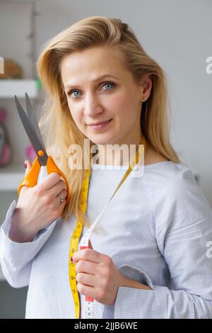 Giovane donna su misura tiene le forbici e regola nelle mani sul posto di lavoro. Concetto di marinaio di professione Foto Stock