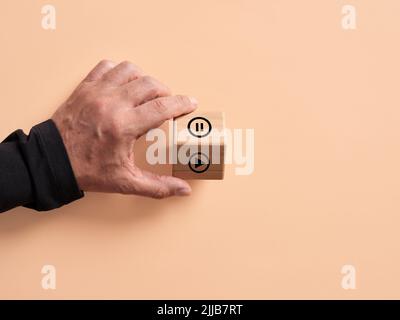 La mano gira il cubo di legno con i simboli di gioco e pausa. La decisione di iniziare o di interrompere. Foto Stock