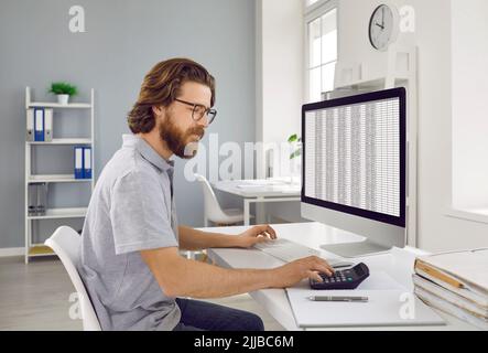 Contabile aziendale seduto al computer dell'ufficio, lavorando con fogli di calcolo e utilizzando la calcolatrice Foto Stock