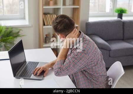 L'uomo stanco sente dolore al collo e alla schiena della testa dopo aver lavorato sul computer portatile Foto Stock