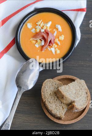 Primo piano di Salmorejo, zuppa di pomodoro fredda e cremosa, servita con prosciutto serrano e uova sode. Tradizionale sfondo di cucina spagnola. Foto Stock