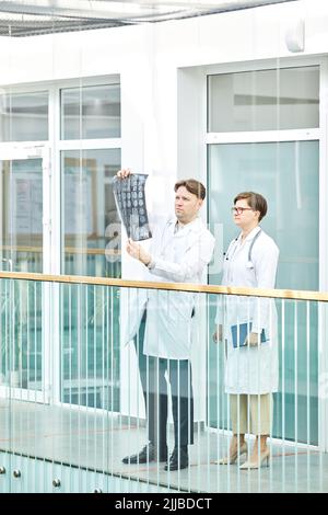 Ritratto verticale a tutta lunghezza di due medici esperti che guardano le immagini radiografiche nella moderna clinica medica Foto Stock