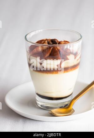 Torta tiramisù classica in un bicchiere su sfondo bianco. Torta di mascarpone a strati. Foto Stock