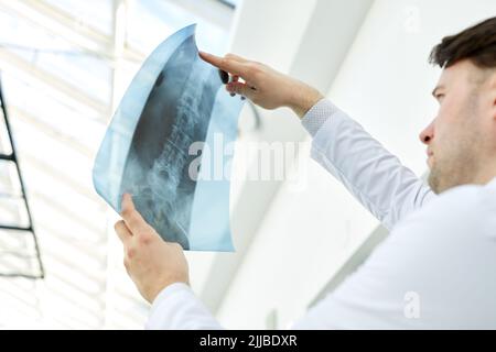 Vista ad angolo basso del medico esperto che tiene l'immagine a raggi X ed esamina lesioni alla colonna vertebrale, spazio di copia Foto Stock