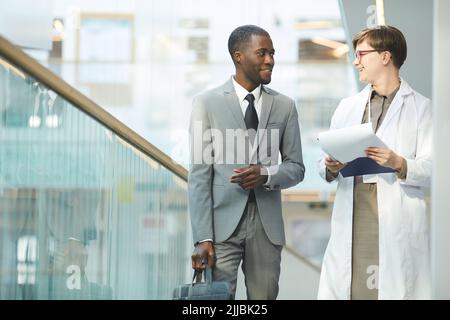 Ritratto di uomo d'affari nero sorridente che parla con una collega, mentre si cammina verso la macchina fotografica nella sala dell'edificio di uffici, spazio copia Foto Stock