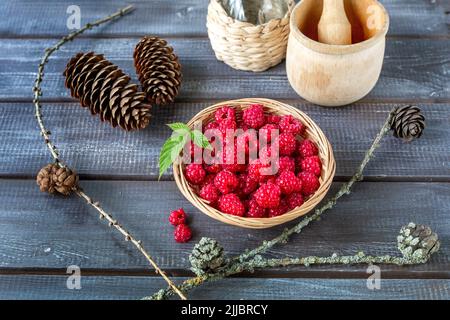 Lamponi freschi in un cestino di vimini per fare marmellata e regali della foresta - coni, rami su un tavolo di legno. Foto Stock