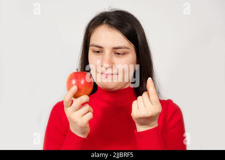 Una donna in rosso tiene una mela e una pillola nelle sue mani. Vitamine in forma naturale e in integratori alimentari sintetici Foto Stock