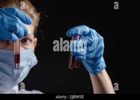 Un virologo femminile lavora con le provette di sangue su sfondo nero. Un'infermiera tiene le provette di sangue nelle mani. Concetto di lavoro su una pandemia Foto Stock