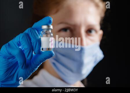 Una donna, un medico o un infermiere, sta tenendo una provetta di medicinale. Medico che tiene una provetta e guanti protettivi blu su sfondo nero Foto Stock