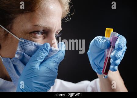 Un medico donna in una maschera medica protettiva guarda i tubi di sangue e piange. Il medico grida quando vede le prove difettose. Il medico è sconvolto e. Foto Stock