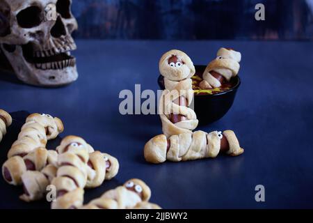 Cibo divertente per i bambini. Hot dog mummy (o maiali in coperta) su un tavolo rustico blu con una ciotola di ketchup e senape tuffo, con ragno web design. Blurre Foto Stock