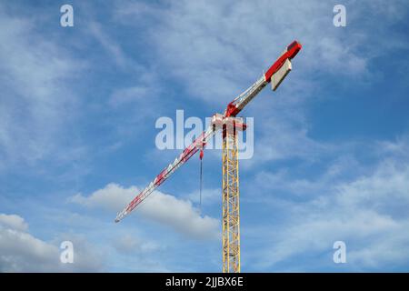 Vista di una moderna gru a torre su sfondo blu cielo nuvoloso - un paranco di strutture edili pesanti per ottimizzare il lavoro di installazione nella costruzione di Foto Stock