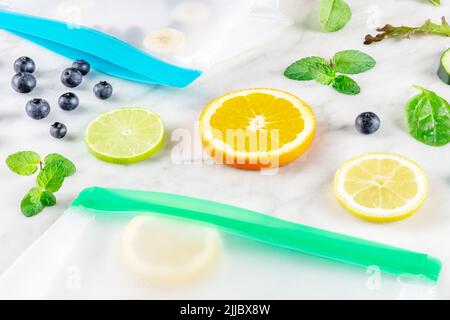 Sacchetti per la conservazione degli alimenti con frutta e verdura, su un tavolo da cucina in marmo bianco. Prodotti freschi estivi in contenitori con chiusura lampo Foto Stock