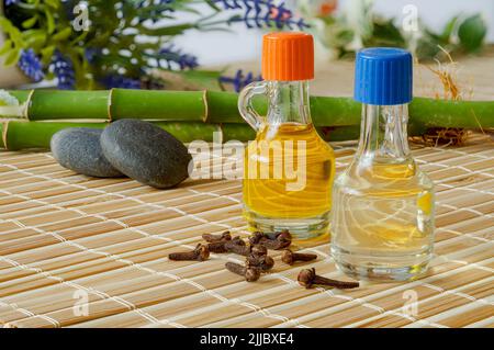 Chiodi di garofano e olio di lavanda. Bambù, ciottoli, fondo di bambù, oli essenziali in bottiglia, concetto di fondo zen, spa Foto Stock