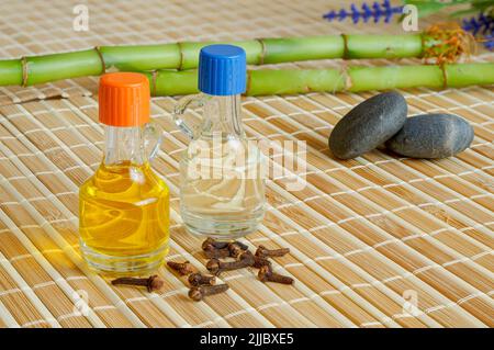 Chiodi di garofano e olio di lavanda. Bambù, ciottoli, fondo di bambù, oli essenziali in bottiglia, concetto di fondo zen, spa Foto Stock