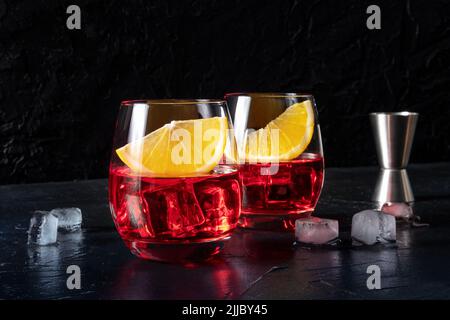 Aperitivo Campari con fette d'arancia fresche e un calice, su sfondo nero. Un cocktail alcolico, due bicchieri e cubetti di ghiaccio Foto Stock