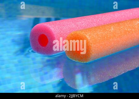 Le vibrazioni estive, i colorati spaghetti in polietilene rosso e arancio galleggiano nella piscina dalle piastrelle blu Foto Stock