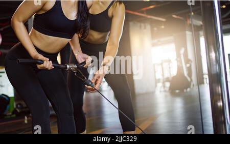 Ragazza sportiva che fa esercizi di peso con l'aiuto del suo personal trainer in palestra. Foto Stock