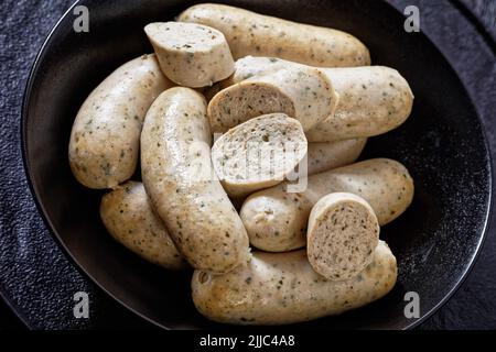 Primo piano di Weisswurst, salsicce bavaresi bianche di vitello tritato, pancetta di maiale, spezie e prezzemolo in ciotola nera Foto Stock