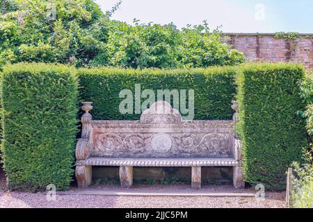 Panca del giardino d'annata scolpita in pietra con decorazioni di foglie di acanthus e rotoli in un angolo appartato di Tatton Park, Regno Unito. Foto Stock